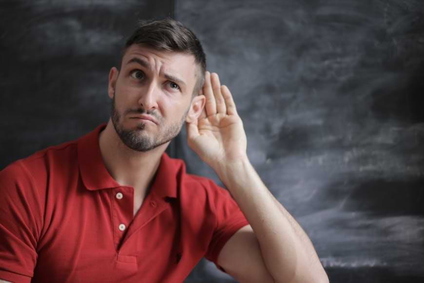 Uomo con la maglietta rossa e la mano all'orecchio nell'atto di ascoltare un rumore. Simbolo di un cliente insoddisfatto che aspetta di essere ascoltato dall'azienda. Un errore da non commettere è quello di non prendersene cura | FullGadgets